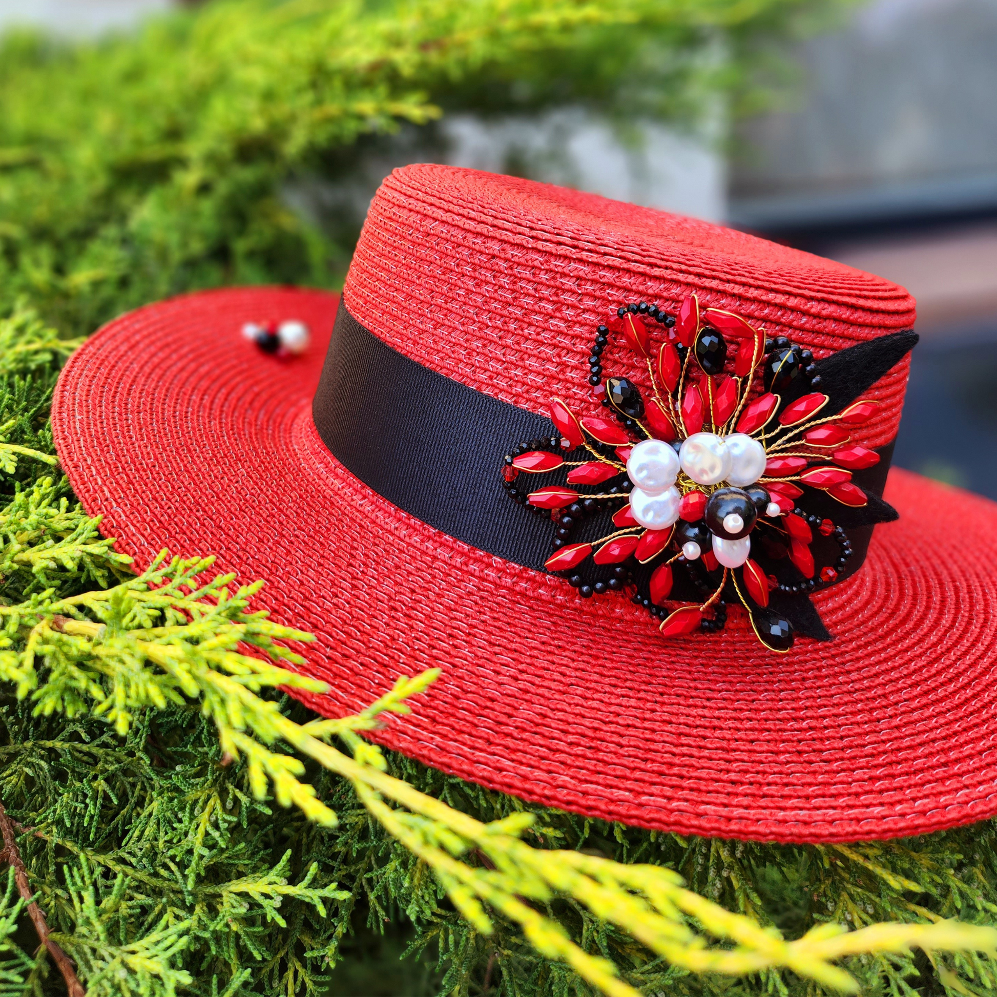 Red Straw Boater Hat with Brooch-a photo of the brooch on the hat, foreground close up.